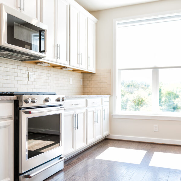 Modern gray, brown neutral kitchen features front cabinets with granite countertops and tile backsplash, window in contemporary home, house, apartment